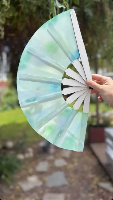 Abanico grande abierto pintado en acuarela verde agua, en un jardín