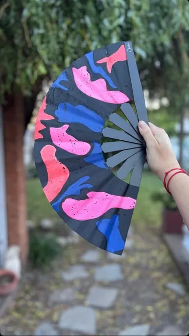 Abanico grande negro con manchas rosas y azules, en un jardín