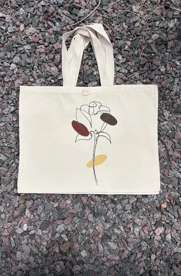 Tote bag de gabardina cruda con una flor dibujada en línea y pétalos bordó, marrón y mostaza