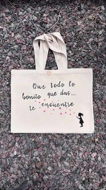 Tote bag de gabardina cruda con la frase "Que todo lo bonito que das te encuentre" y una nena soplando estrellas