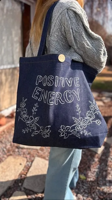 Tote bag de jean con la frase "Positive Energy" y flores pintadas en blanco