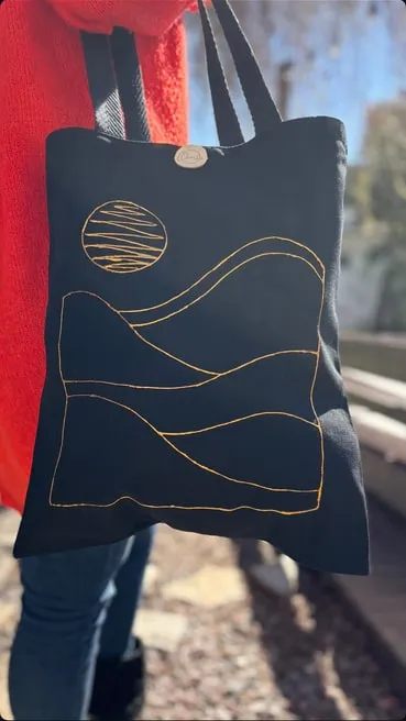Tote bag chica negra con un paisaje de líneas doradas y una luna